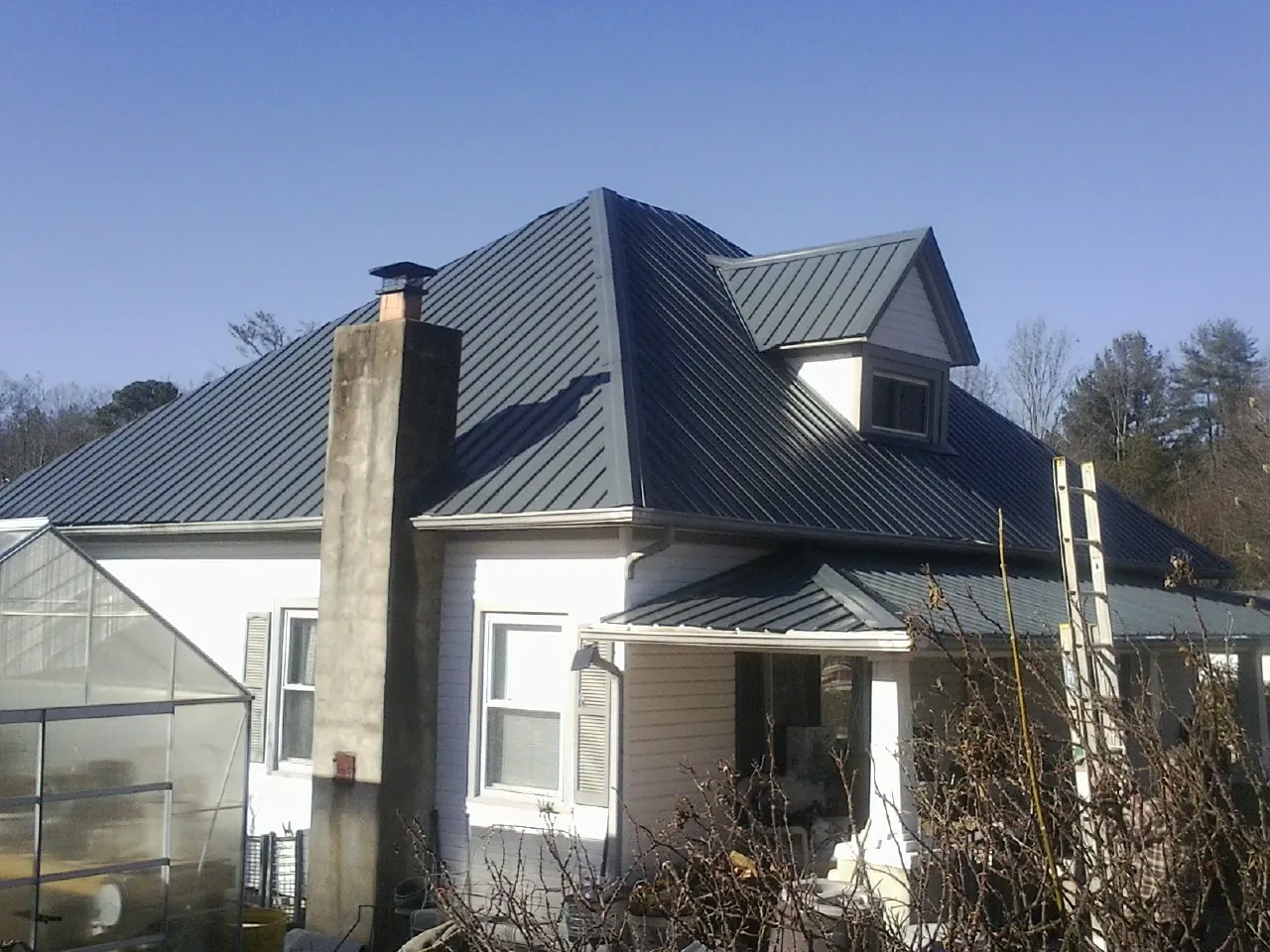Dark blue standing seam metal roof on a white farmhouse with dormer — Slate & Tile Roof Repair by Roofing Brothers in Plain City