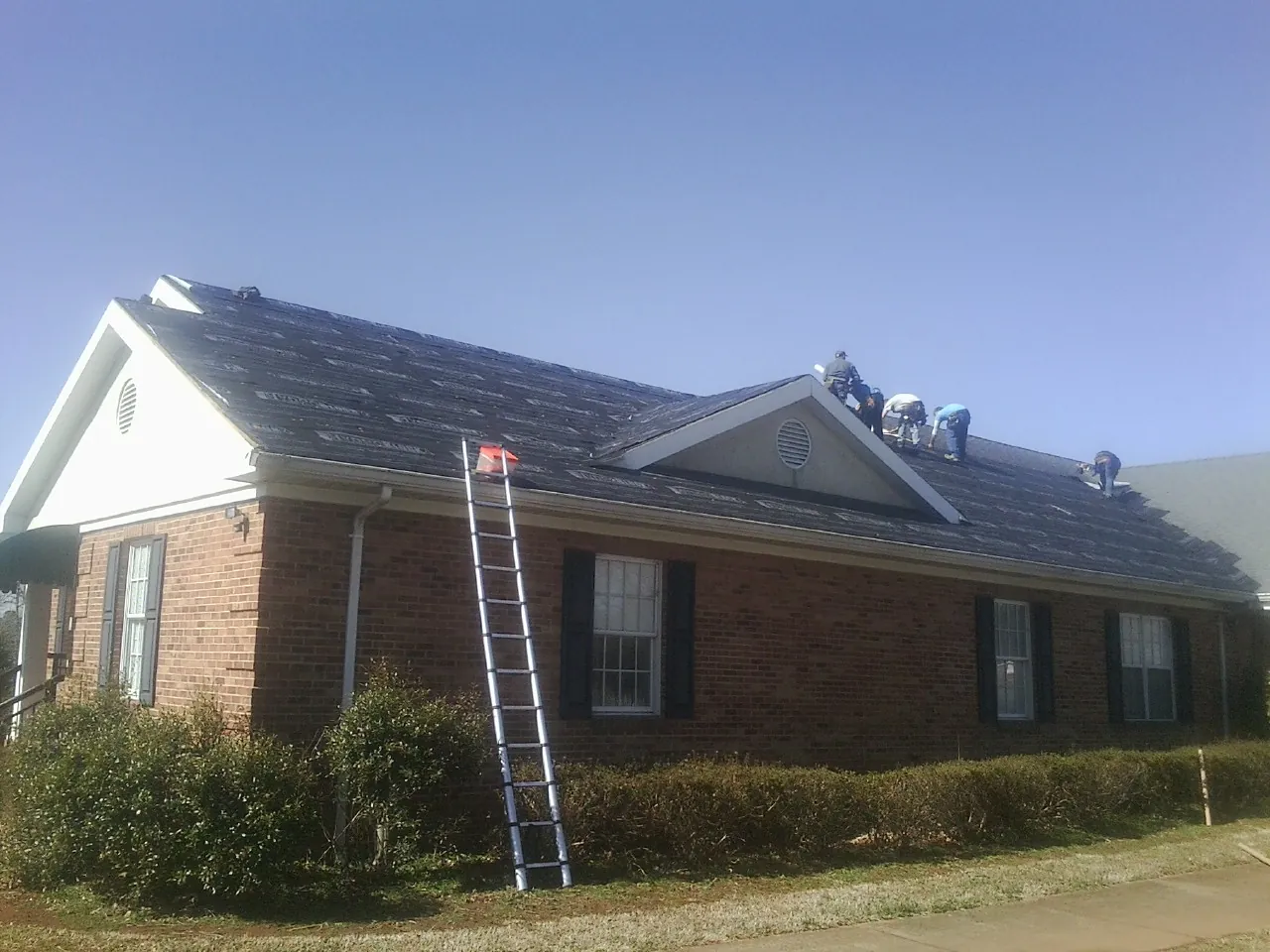 Crew tearing shingles off a brick ranch roof with a ladder set — Emergency Roof Repair work by our crew in Plain City