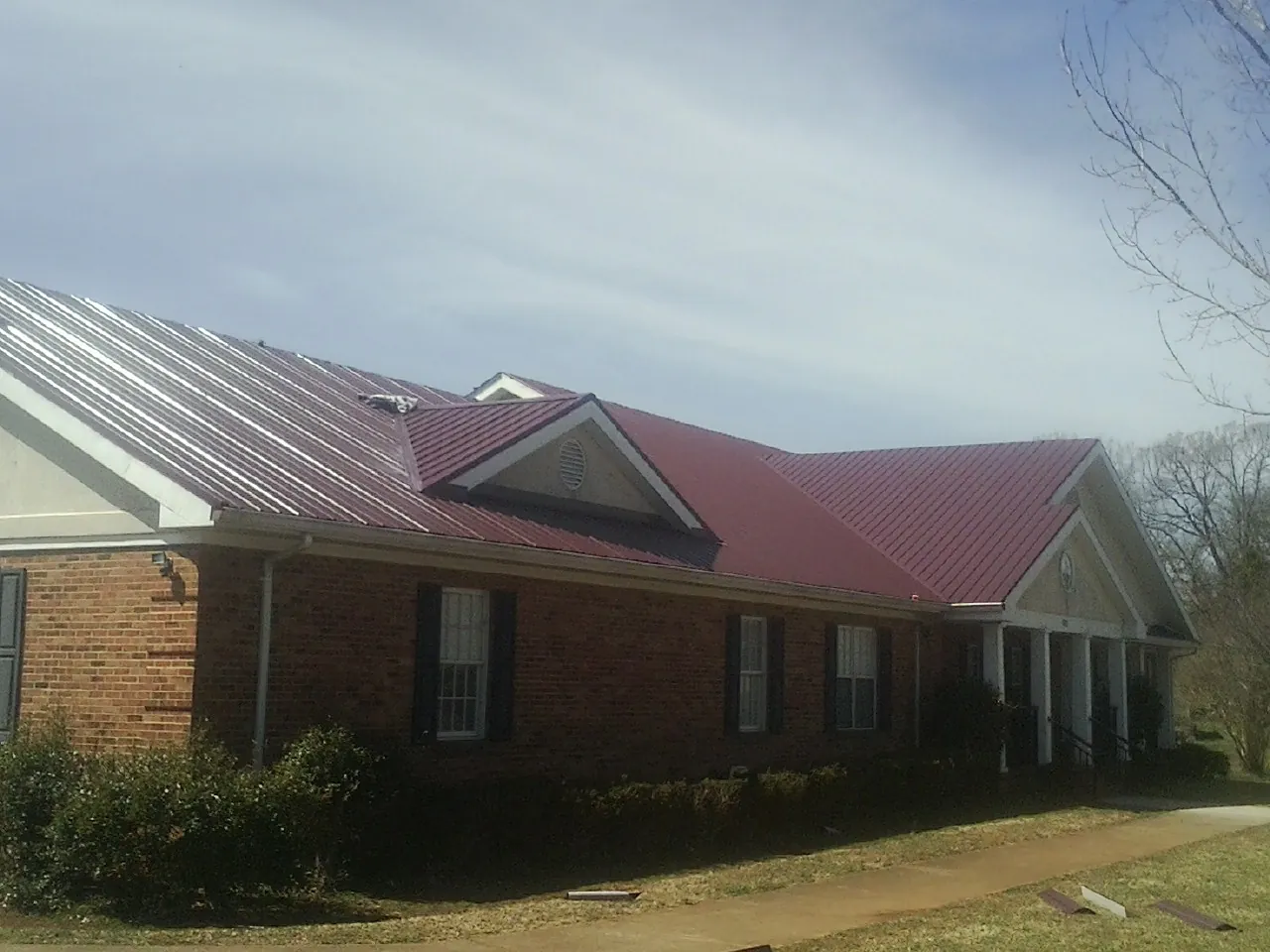Red metal roof with gabled entries on a long brick building, from a Hail Damage Roof Repair job in Plain City