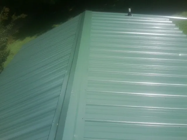 New green metal panels meeting at the ridge of a roof — Flat Roof Repair work by our crew in Plain City