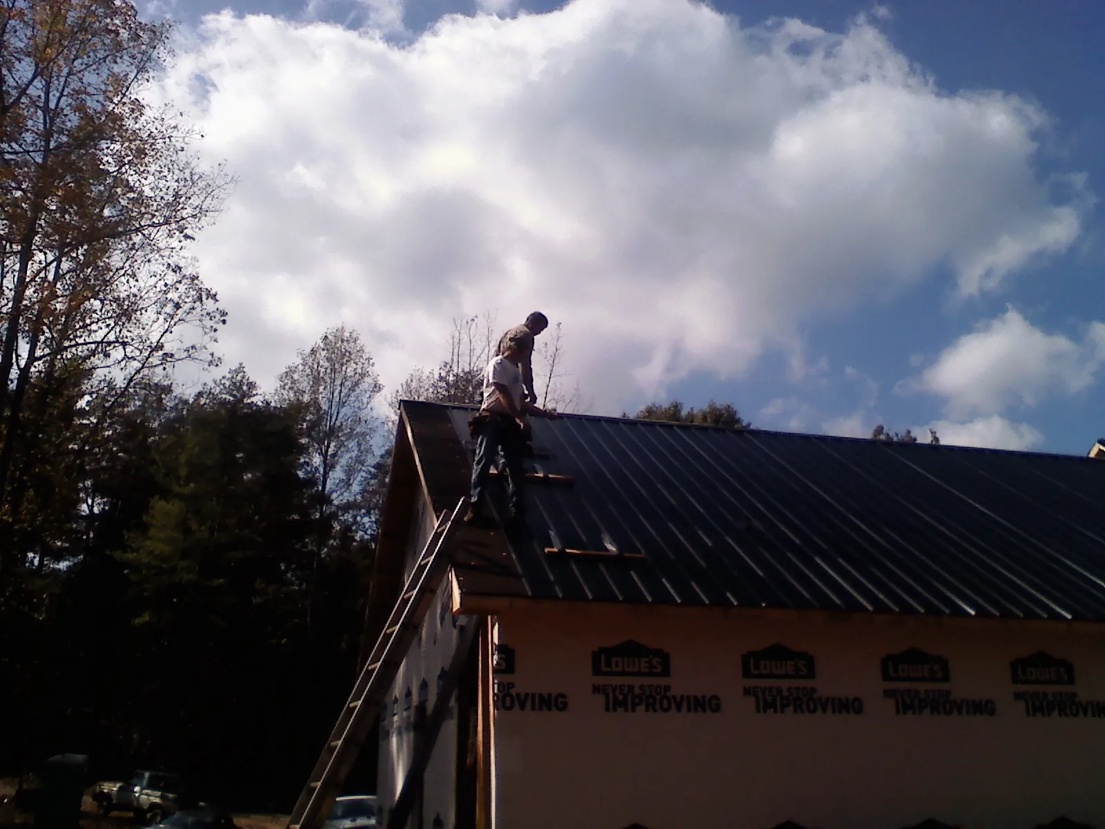 Roofer fastening dark metal panels high against a cloudy sky, from a Roof Inspection job in Plain City