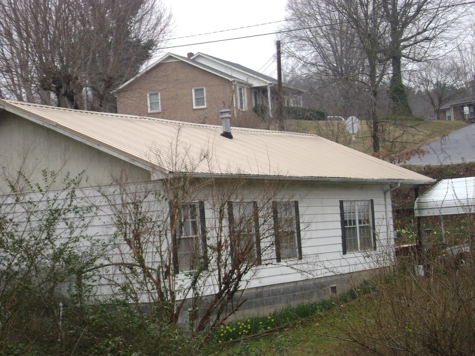 Tan metal roof on a white sided house set into a hillside — Commercial Roofing by Roofing Brothers in Plain City